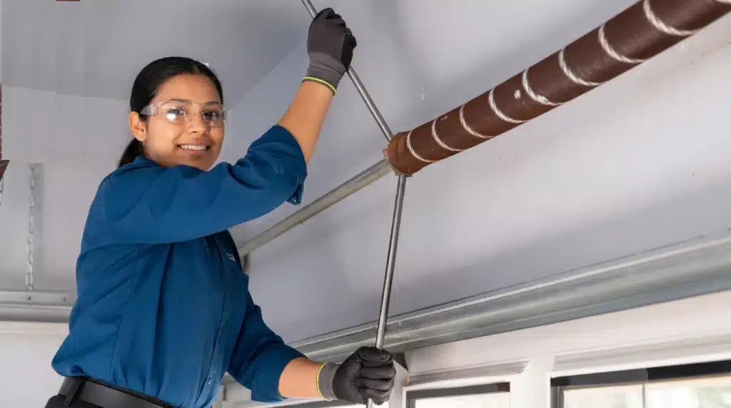 Professional technician winding garage door torsion spring with steel bars.