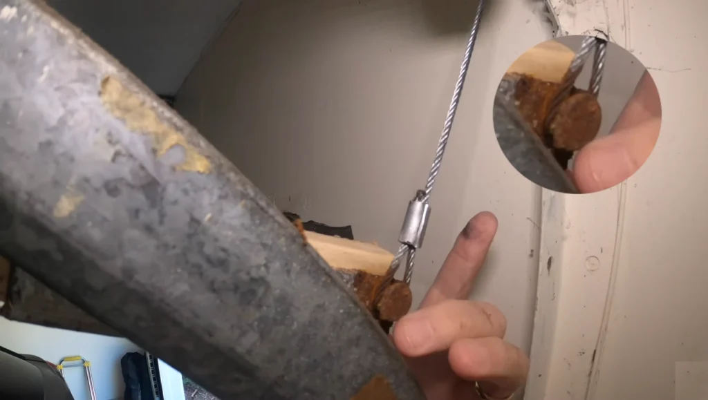 Close-up of a rusted and frayed garage door cable attached to a bottom bracket, showing common corrosion failure.