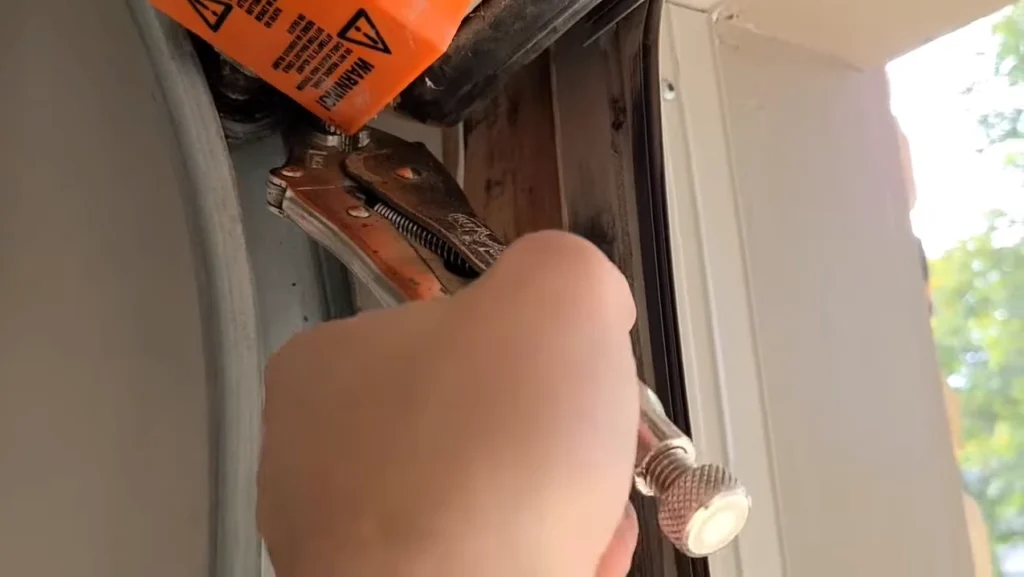 Close-up of a metal vice grip secured to the vertical garage door track under a roller for safety during a broken garage door cable repair.